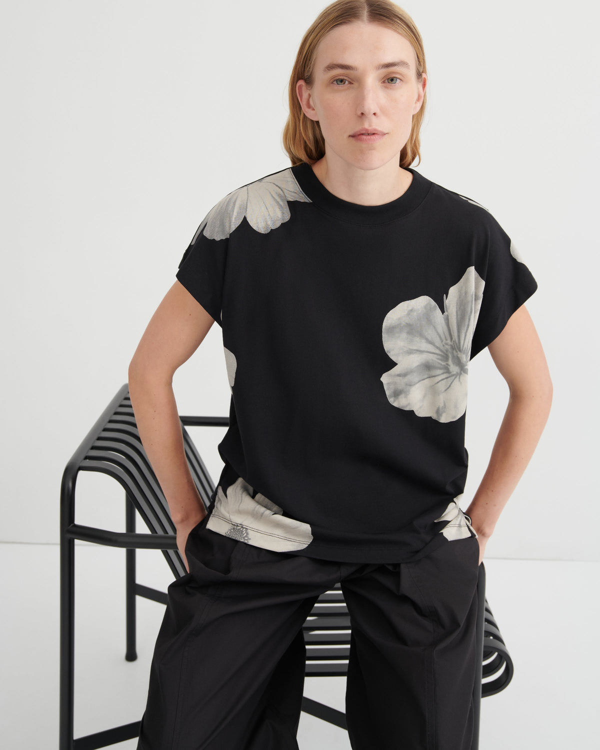 Person wearing a black t-shirt with floral designs sitting on a chair against a white background