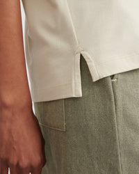 Close-up of a person wearing a light beige short-sleeve top and an olive green textured skirt or trousers, showing the hem detail and fabric texture.