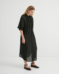 A woman modeling a loose, olive green midi dress with short flutter sleeves, a gathered high neckline, and a draped silhouette, paired with dark brown flat shoes against a plain white studio background.