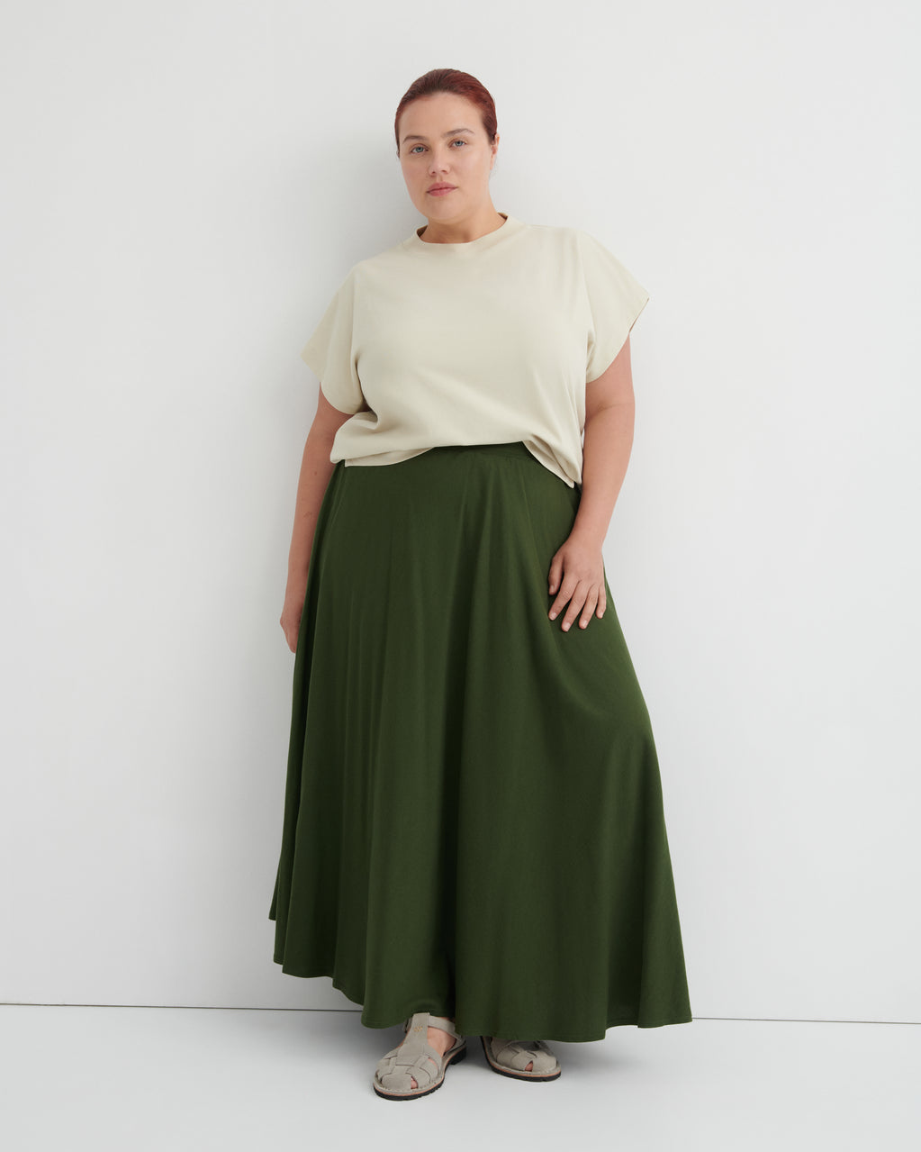 Person wearing a beige top and green skirt on a white background
