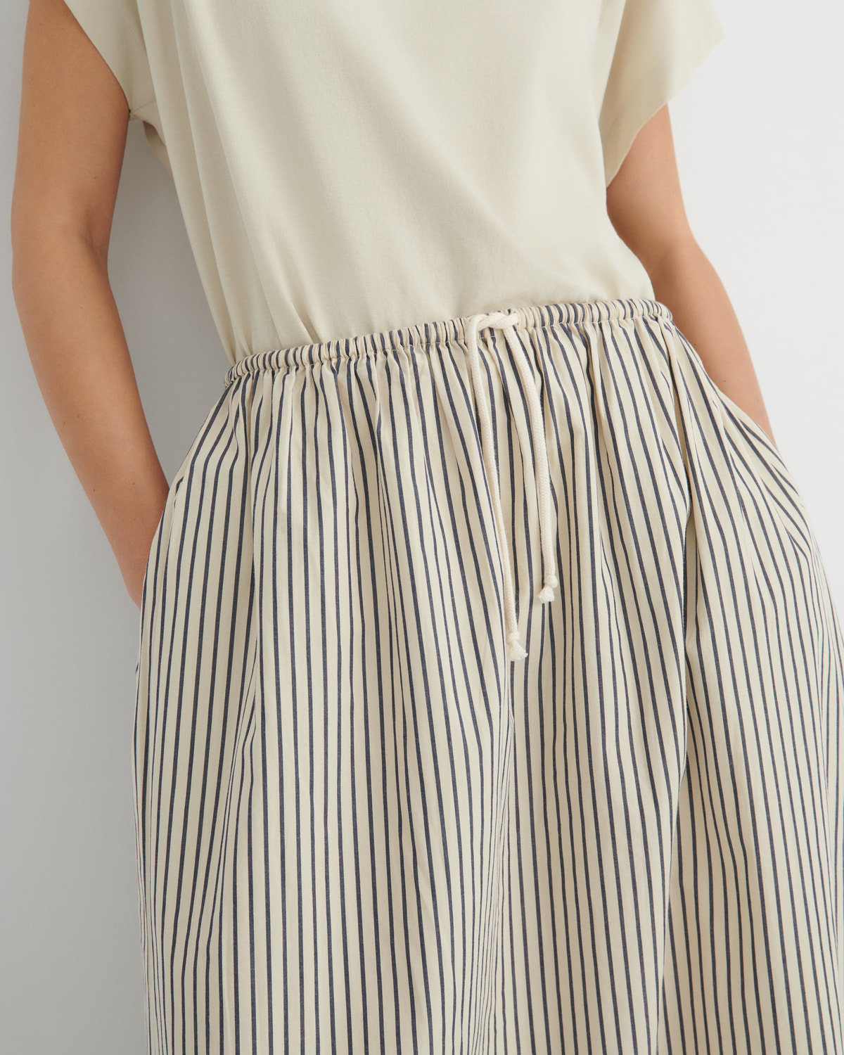 Close-up of a person wearing a cream sleeveless top and loose striped wide-leg pants with an elastic drawstring waist, against a light gray background.