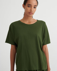 A woman wearing a loose, short-sleeve crew-neck t-shirt in olive green, photographed against a clean light gray studio background.