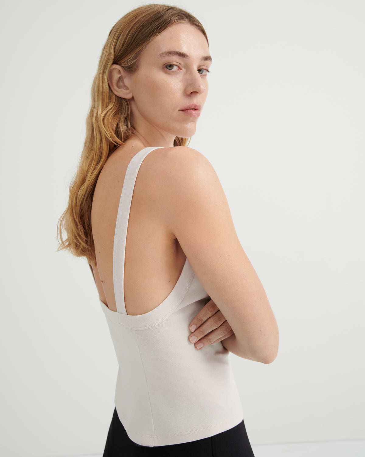 A woman wearing a fitted white tank top with wide shoulder straps and a scoop neckline.