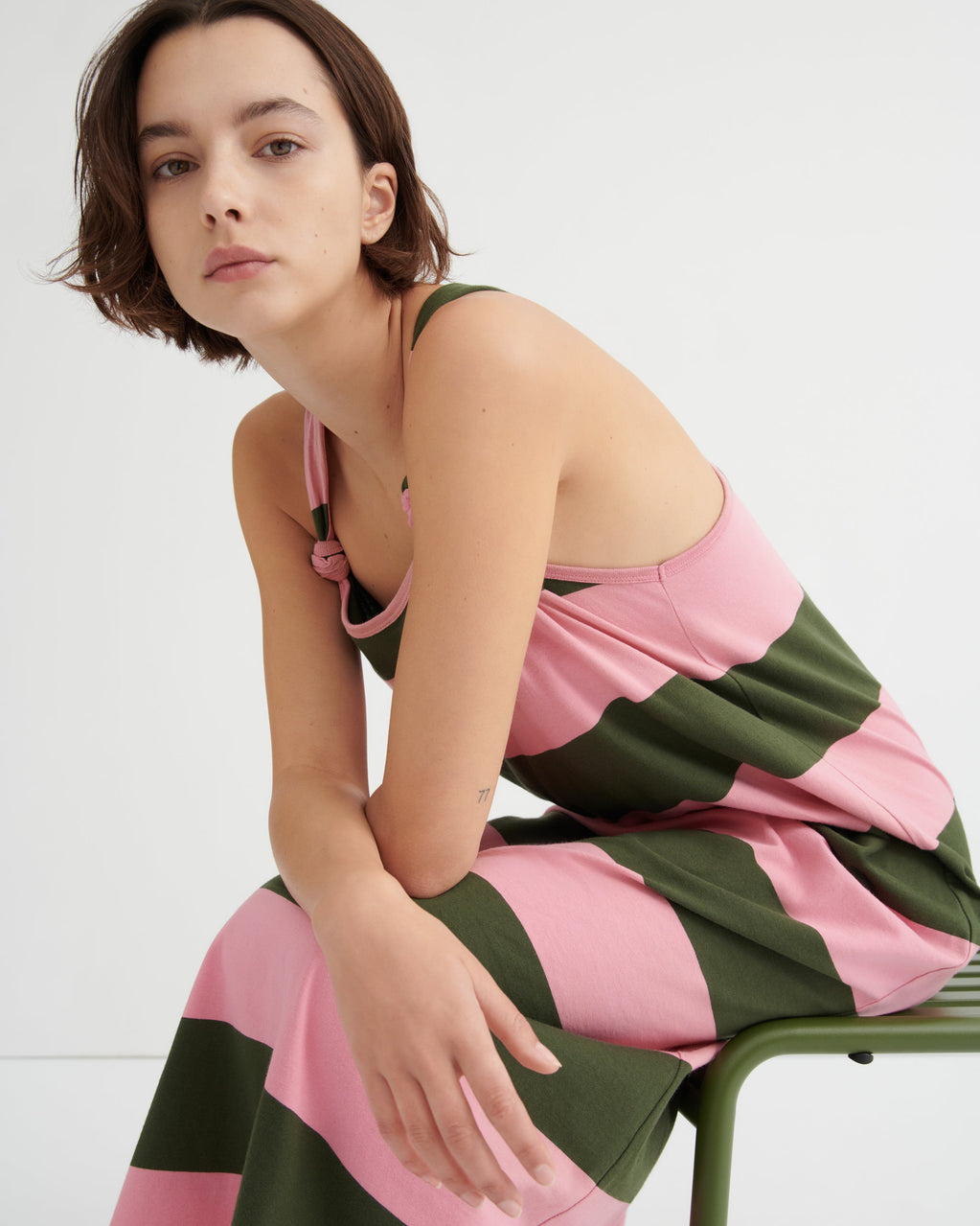 Woman wearing a pink and green striped dress sitting on a chair against a white background