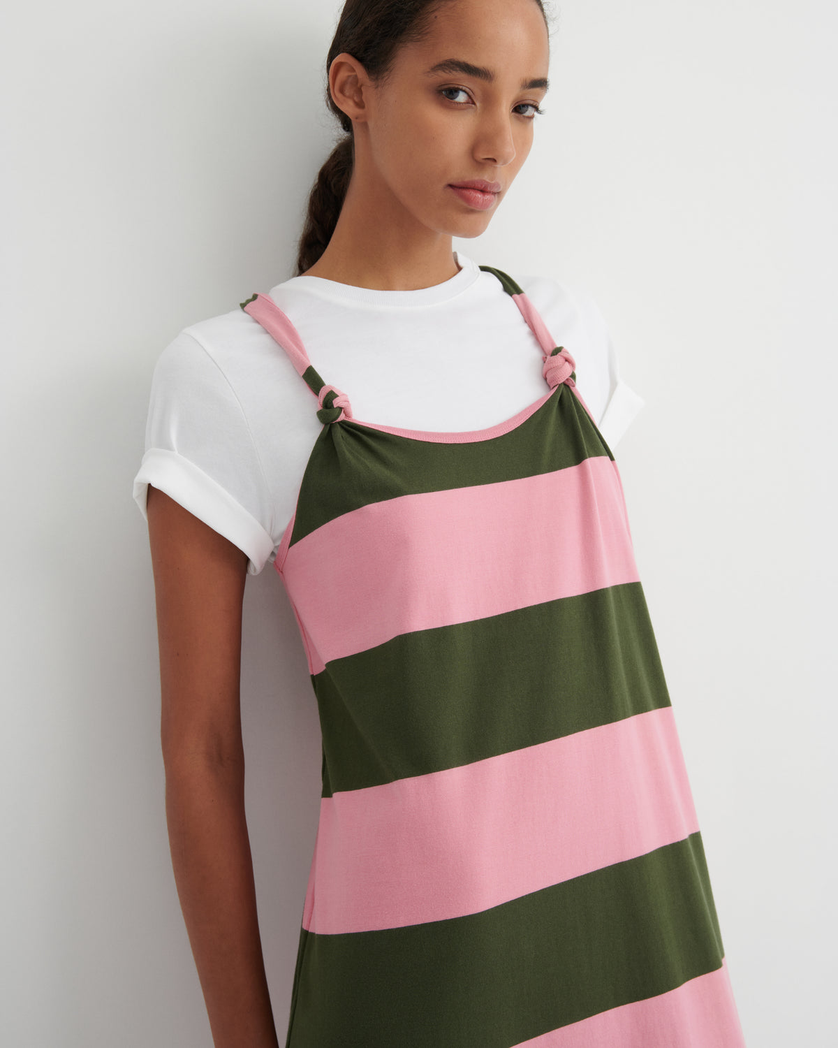 Woman wearing a white t-shirt and a green and pink striped apron against a white background