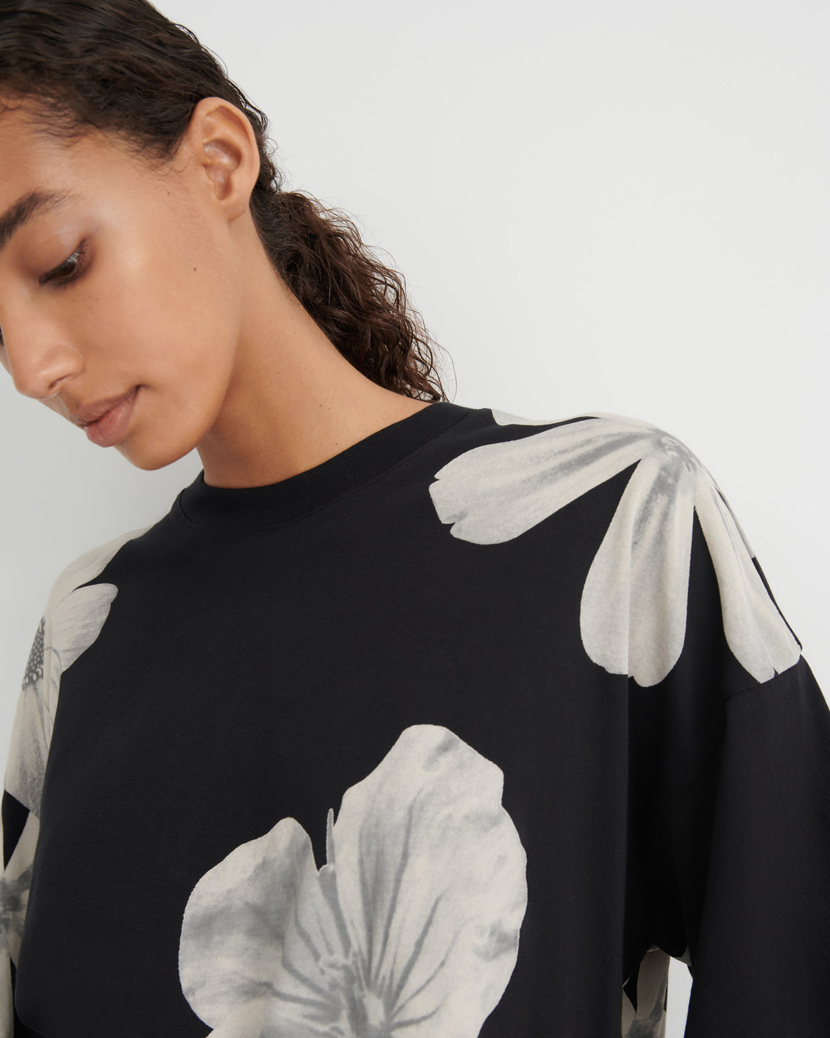 A close-up of a model wearing a black crewneck sweatshirt with a large, light gray floral print on the front and shoulders.