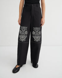 Black pants with white floral embroidery on a white background
