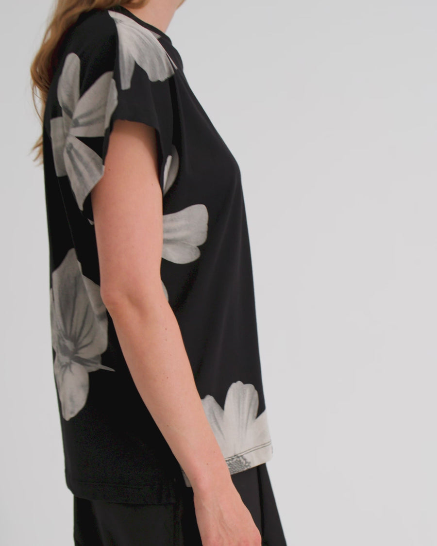 A women wears a sleeveless black tee with big white floral motifs and black pants.