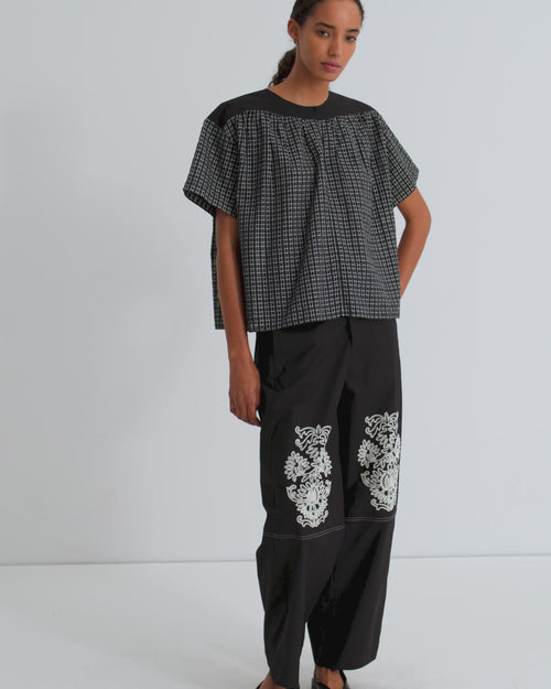 A women wearing a mini check black short sleeve tee and black pants with floral embroidery on the knee.