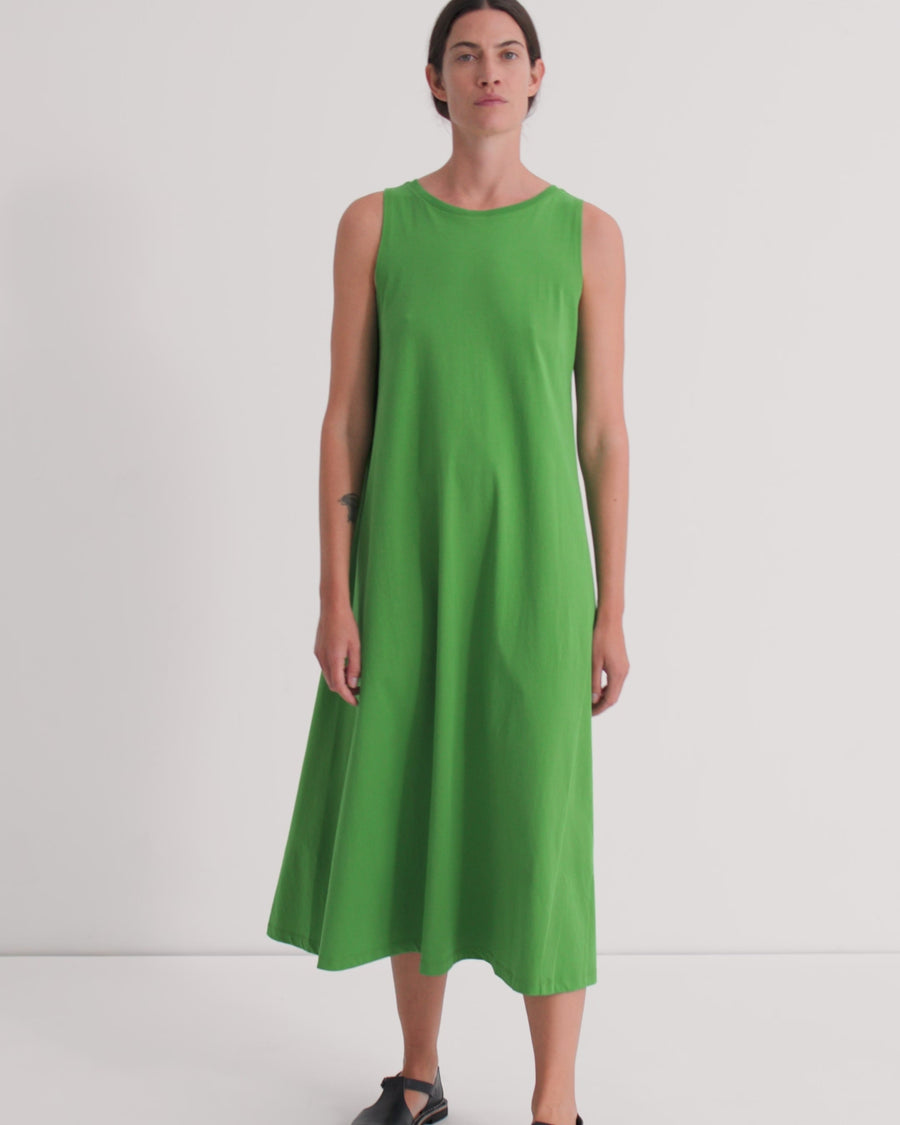 A women wearing a vivid green sleeveless midi dress against a grey background.