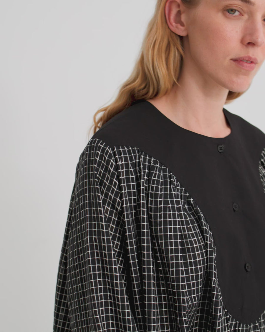 A women wears a black mini check dress with a black yoke against a white backdrop.