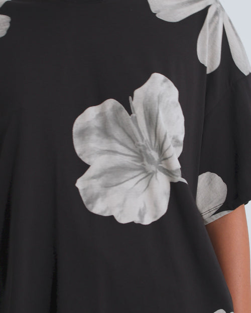 A model wearing an oversized boxy tee in black with white florals and black shorts.