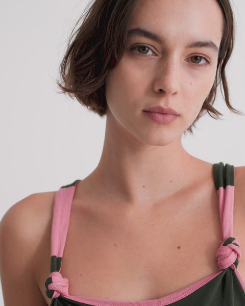 A women wearing a halterneck knotted dress with dark green and pink stripes.