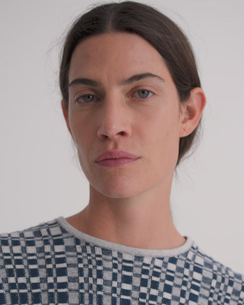 A women wears a check knit tee and dark denim shorts.