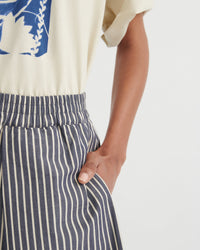 Person wearing a white shirt with a blue design and striped pants on a light background