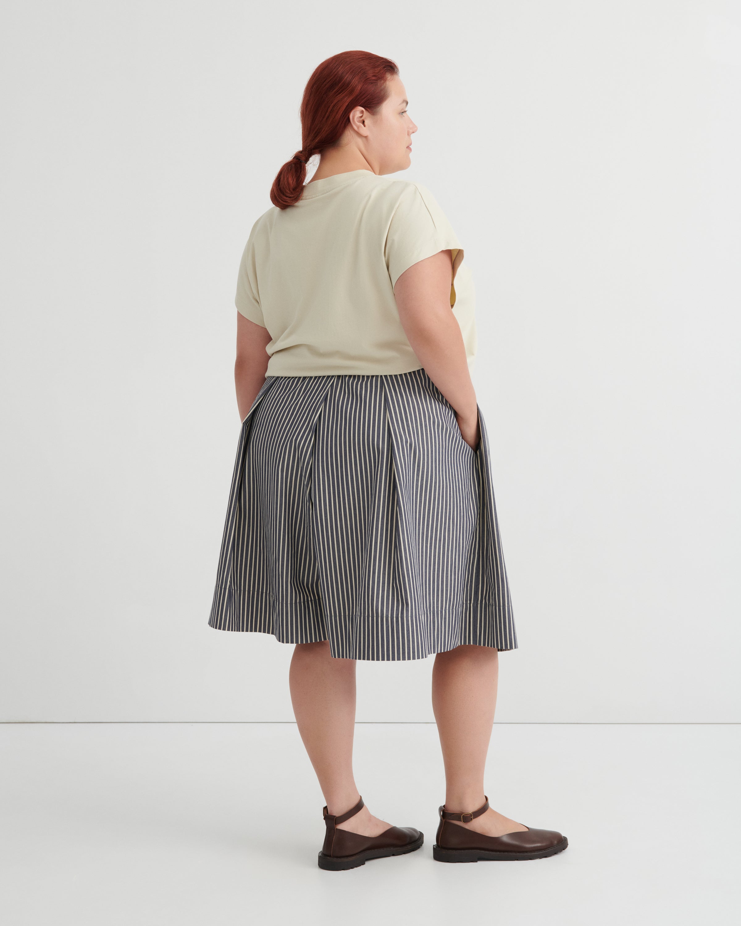 Person wearing a light green shirt and striped skirt on a white background