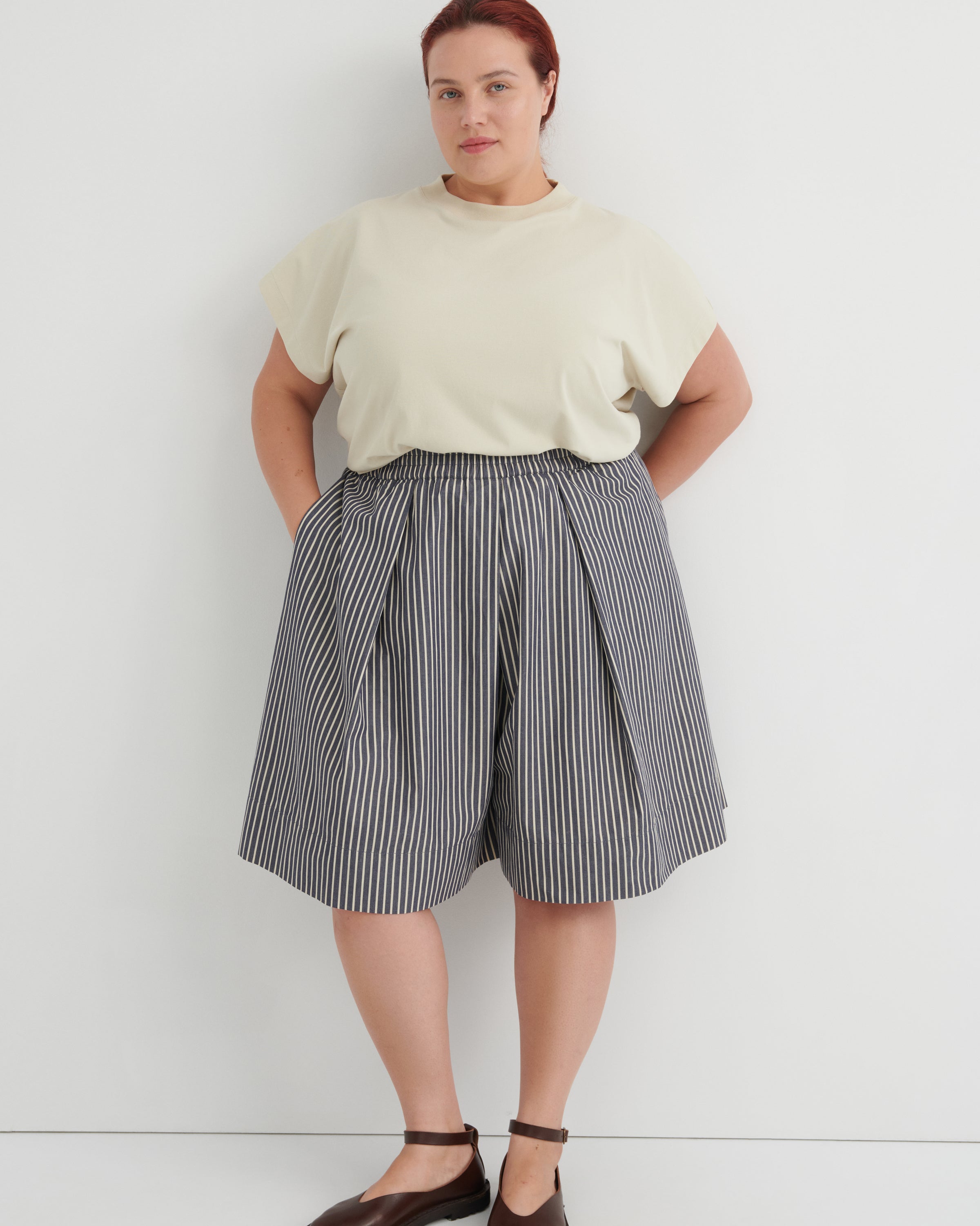 Person wearing a light-colored top and striped skirt against a white background