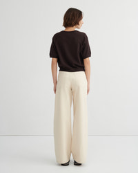 A model shown from the back wearing a dark brown short-sleeve top and cream wide-leg trousers against a light gray studio background.