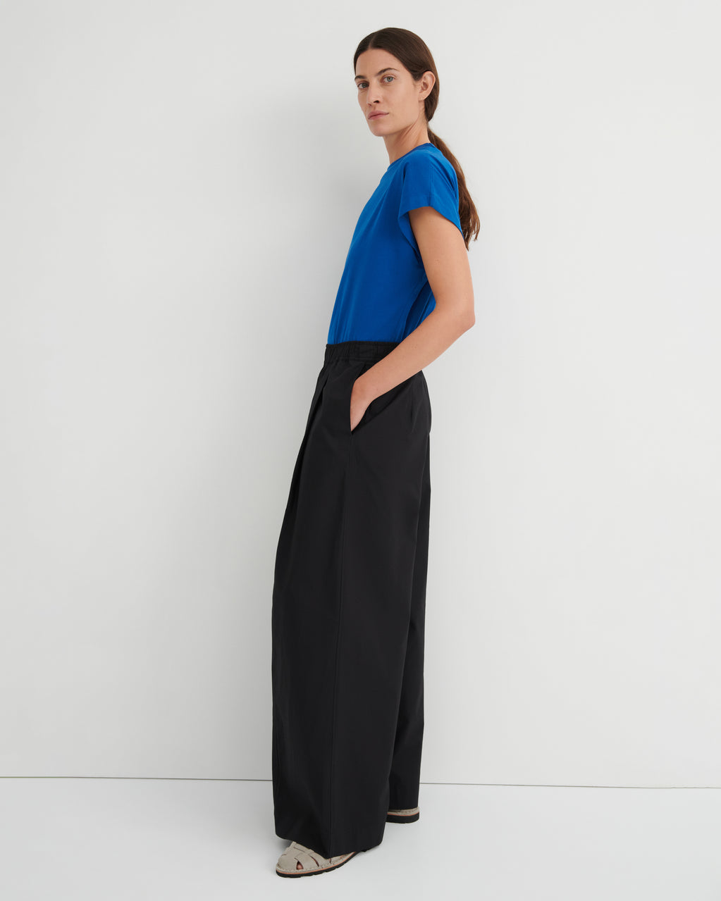 Woman wearing a blue top and black wide-leg pants against a white background