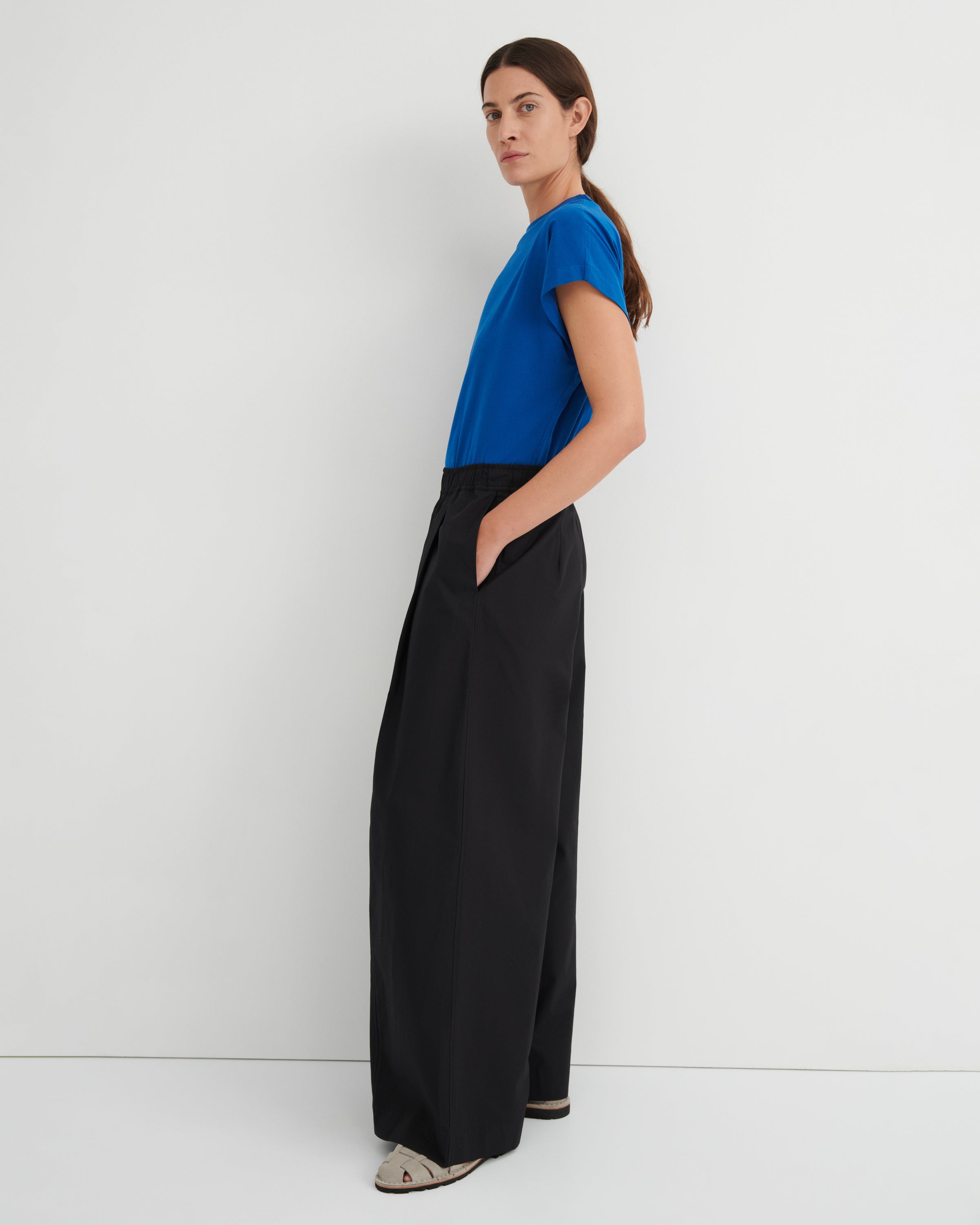 Woman wearing a blue top and black wide-leg pants against a white background