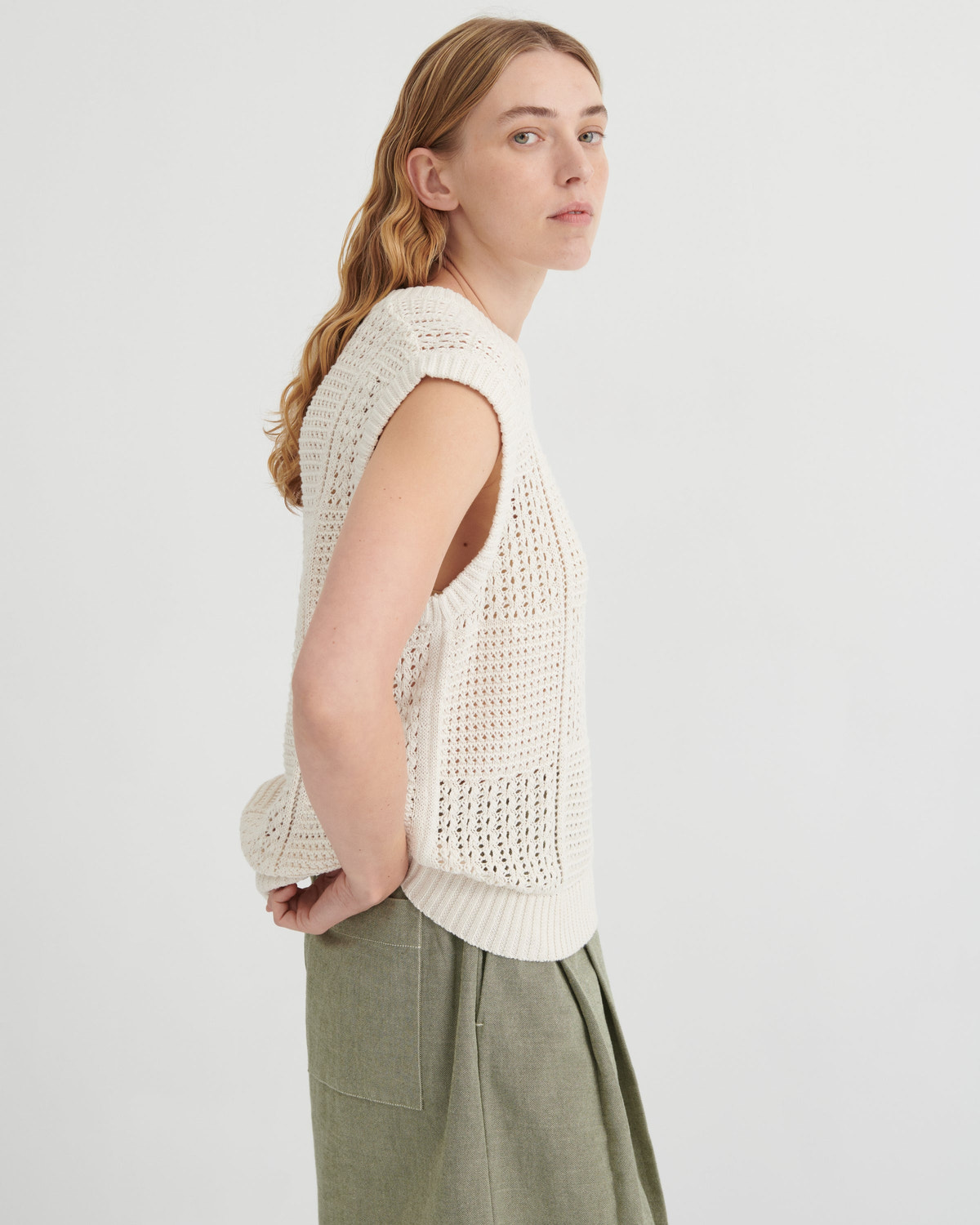 Woman wearing a white knitted vest and green pants on a light gray background