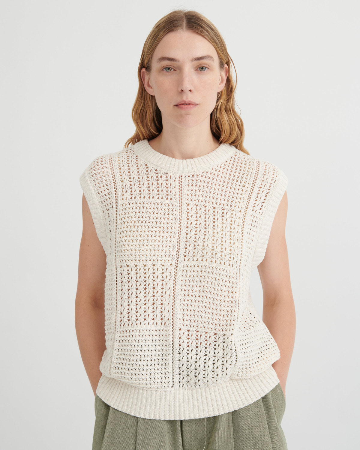 Woman wearing a white sleeveless knitted top against a plain background